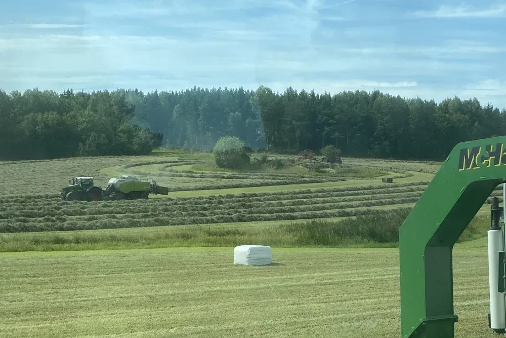 Traktor och balpress på ett fält med hösilagebalar